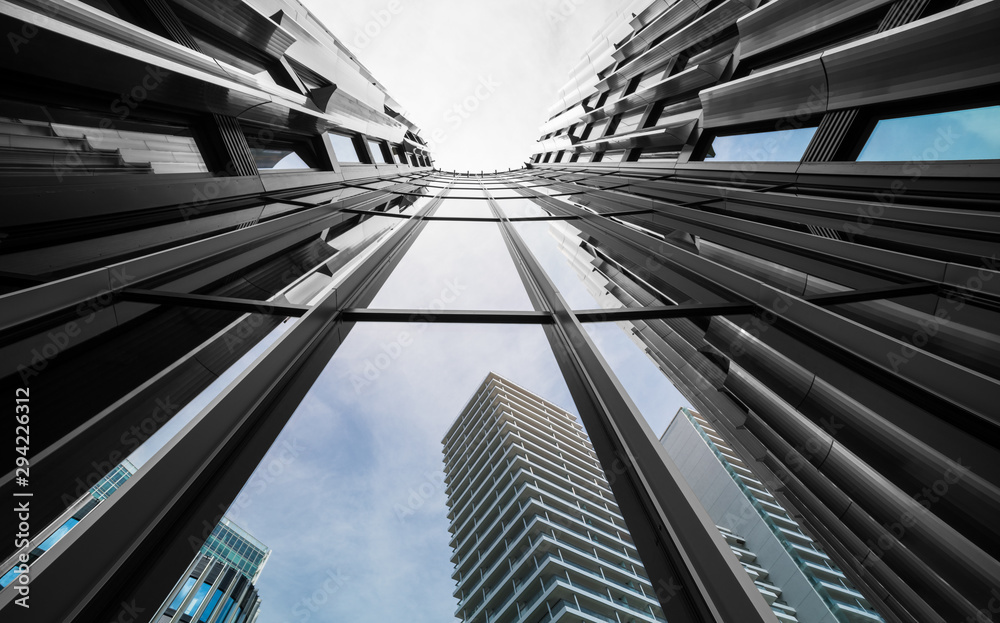 Obraz premium Facade detail of modern high-rise building from below. Mirroring of concrete skyscrapers on blue sky in shiny glass windows. Artistic architectural background of Prague, capital of the Czech Republic.