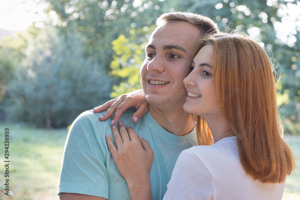 Fototapeta premium Young teenage couple outdoors. Pretty girl with red hair and handsome boy hugging together.