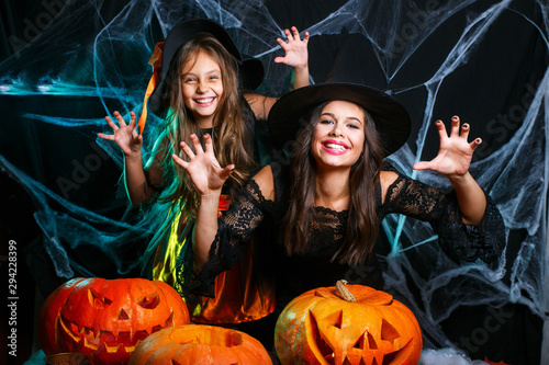 Cute little girl and mom in witch hats are looking at camera and having fun on black Halloween background