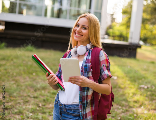  Female student with headphones using digital tablet outdoor.