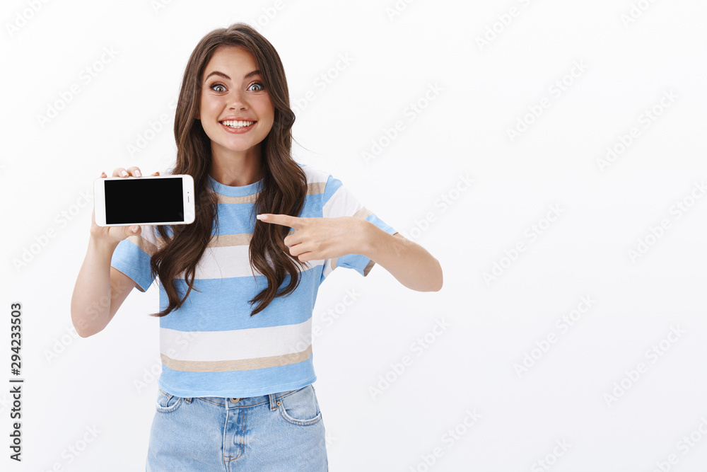 Cheerful impressed enthusiastic young woman cannot wait play new smartphone game, hold mobile phone, pointing horizontal screen and smiling astonished, promoting cellphone app