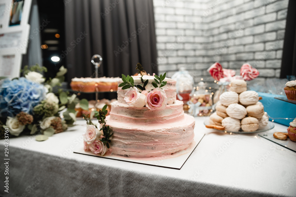 Wedding ceremony. Beautiful cake on the table. Elegant pink wedding cake decorated with roses with candy bar on background Wedding ceremony. Beautiful cake on the table. Elegant pink wedding cake decorated with roses with candy bar on background