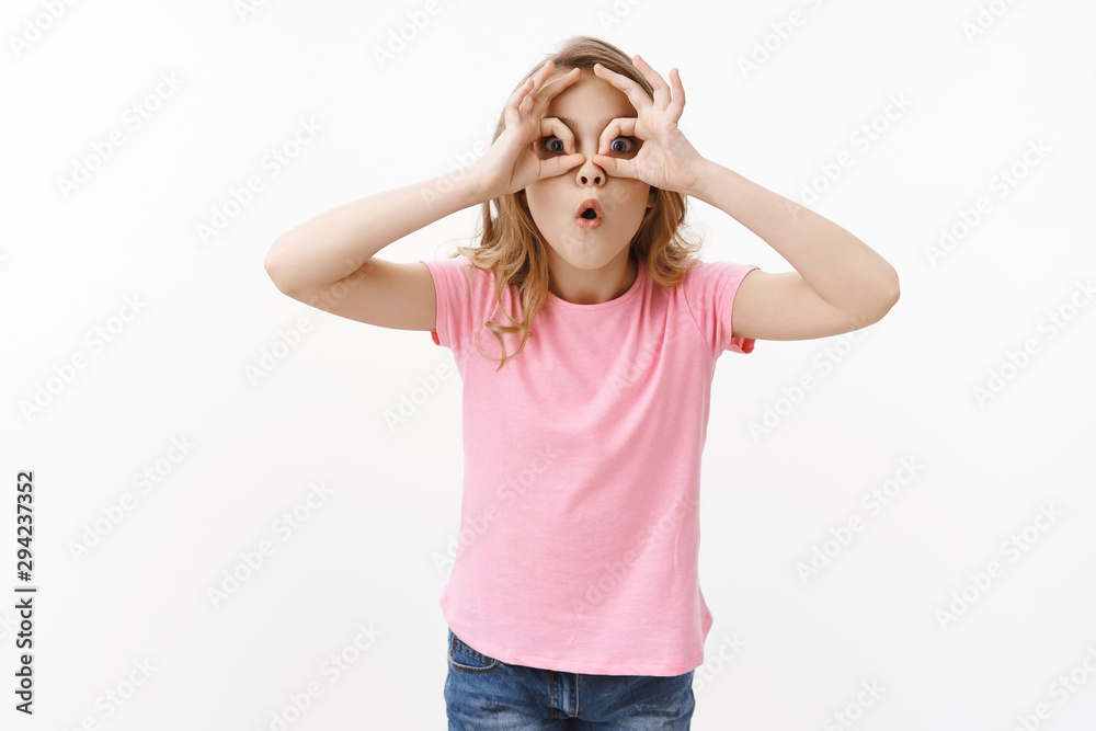 Surprised and amused cute little fair haired girl checking out amazing cool new toy, look through finger circles like binocular, stare forward astonished excited see awesome product copyspace Surprised and amused cute little fair haired girl checking out amazing cool new toy, look through finger circles like binocular, stare forward astonished excited see awesome product copyspace