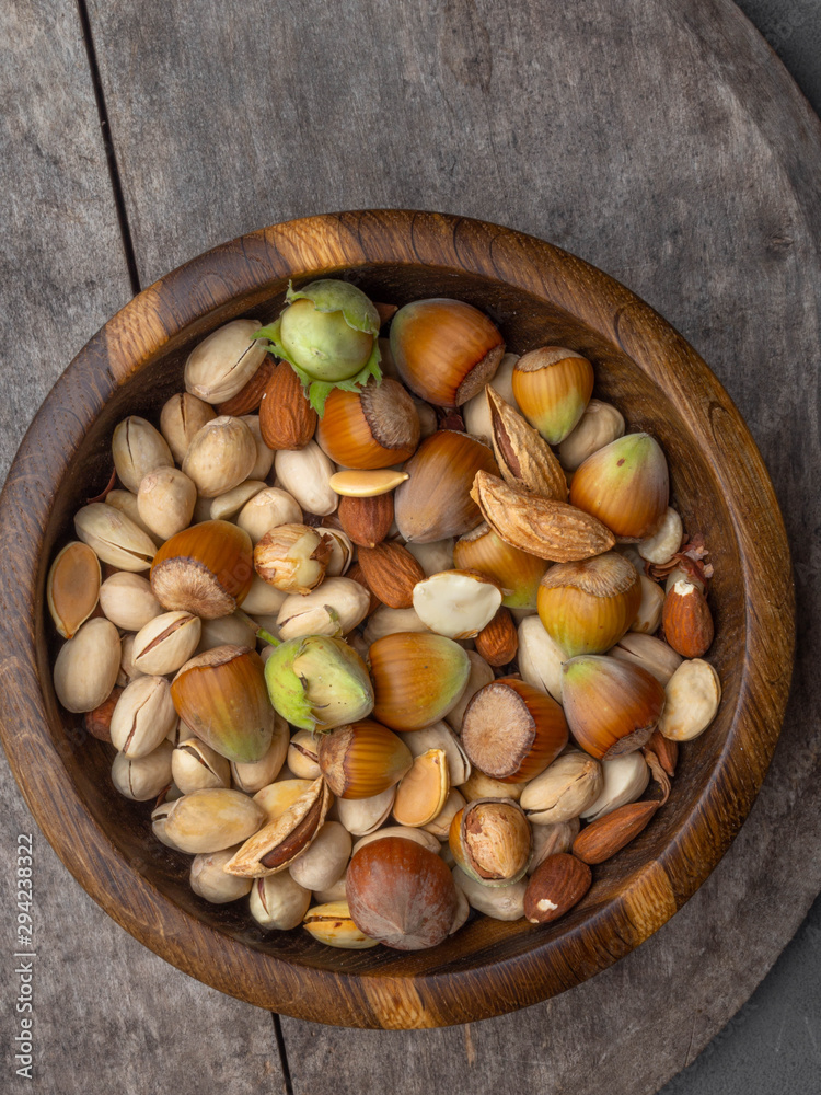 Wooden bowl with mixed nuts on wooden surface. Healthy food and snack. Pistachios, almonds, hazelnuts and seeds, rich with magnesium, vitamin E