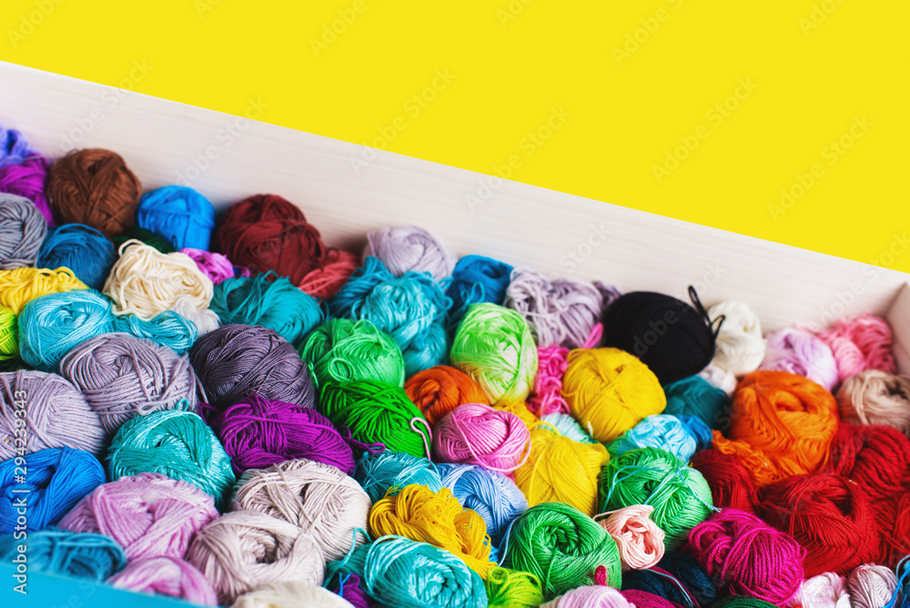 Сrocheting and knitting. Colorful multicolored skeins of yarn in the box on a yellow background. Women's hobby.