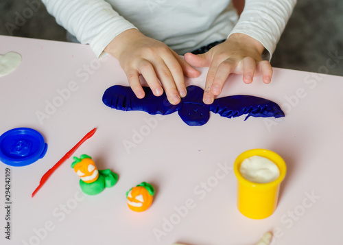 child sculpts from plasticine pumpkins and decorations for the holiday of Halloween. Kids hands with colorful clay or plasticine. photo