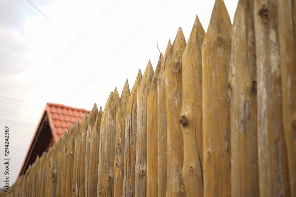 Fototapeta premium Fence made of sharp wooden stakes and red tiled roof under blue sky