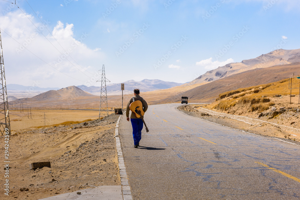 A man with a guitar walks along the road on the Tibetan plateau. Tibet. China