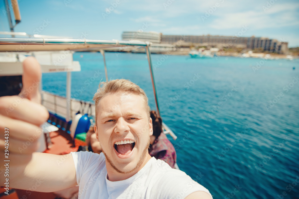 Traveler man takes selfie photo on cruise liner, ship for traveling through Mediterranean Sea, hand gesture thumb up