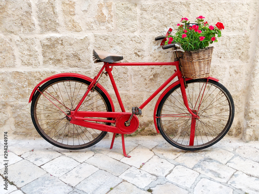 Red bicycle with flower basket agains old stone wall on italian city street