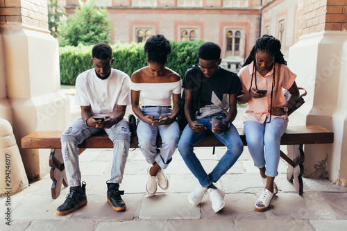Group of african students social networking using several tech devices outdoors