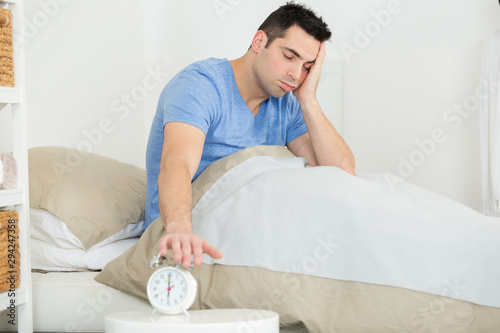 sleepy man in bed turning off his alarm clock