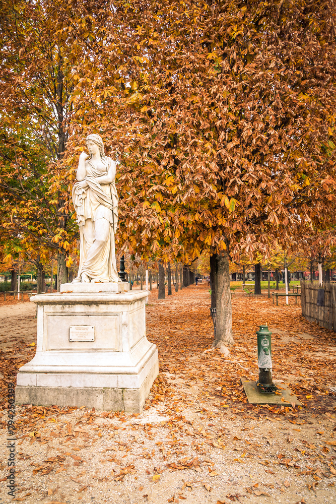 Fototapeta Alley of the Jardin des Tuileries covered with orange autumn leaves, statue in the Tuileries garden in Paris France on a beautiful Fall day