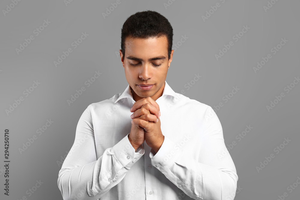 Young African-American man praying on grey background Young African-American man praying on grey background