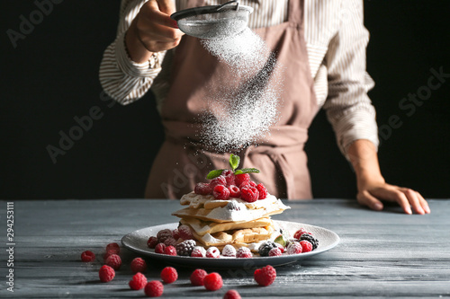 Woman sprinkling sugar powder onto Belgian wafers on table