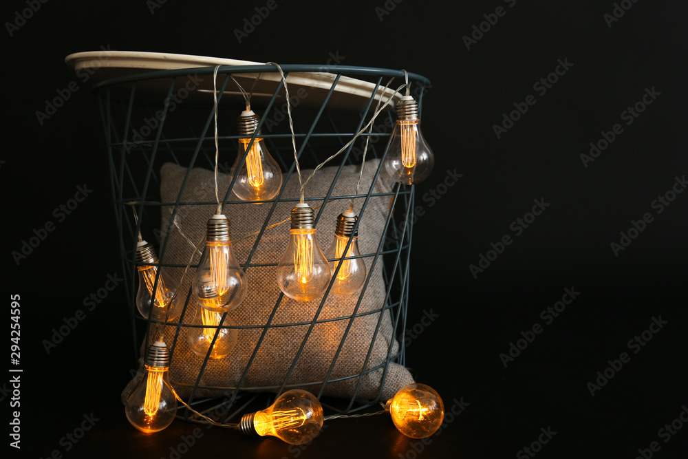 Basket with glowing garland and pillow on dark background