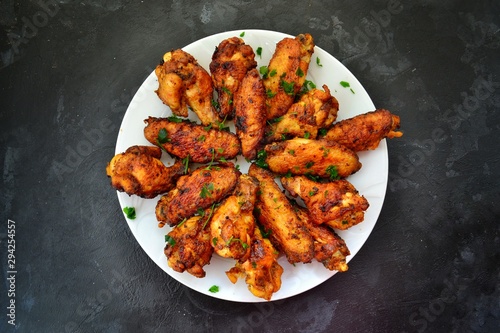 Fried chicken wings. Chicken wings on a dark background. Barbecue meat, grill. Sauce in bowls, ketchup, mayonnaise, mustard, cheese sauce. Appetizing fried meat in the white plate. bowl.