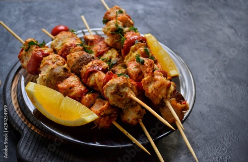 Appetizing food on a dark background. Chicken skewers with mushrooms and tomato. Oven skewered chicken fillet. Chicken kebab on the wooden board and black plate.