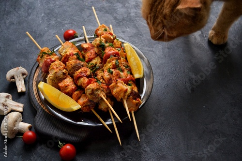 Appetizing food on a dark background. Chicken skewers with mushrooms and tomato. Oven skewered chicken fillet. Chicken kebab on the wooden board and black plate.