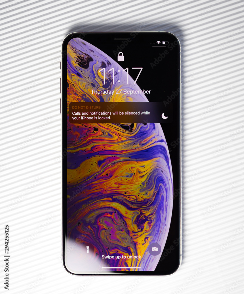 Foto Stock PARIS, FRANCE - SEP 27, 2018: new iPhone Xs Max smartphone model  by Apple Computers close up with lock screen and wallpaper against stripes  white background do not disturb | Adobe Stock