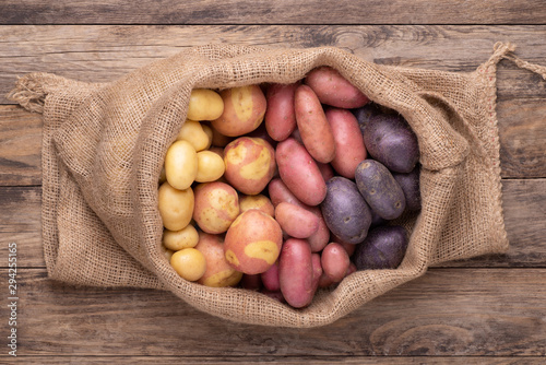 Fotografie Different types of potatoes in a sack on wooden rustic table