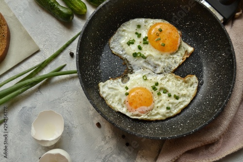Tasty breakfast. Food on the table. Food on a light gray decorative background. Fried eggs in a pan. Eggs, green onions, brown bread, cucumbers.