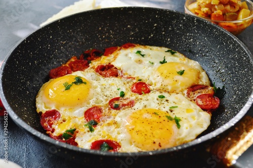 Fried eggs with tomatoes and parsley. Fried eggs in a black pan on a dark background. Scrambled Egg Ingredients