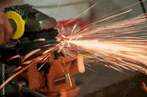 Worker in a workshop grinder processes metal, from which hot bright sparks fly in different directions