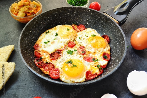 Fried eggs with tomatoes and parsley. Fried eggs in a black pan on a dark background. Scrambled Egg Ingredients