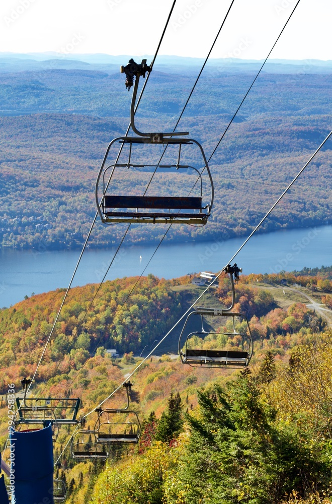 Chair lift on cables above a lake and fall trees