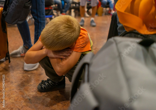 blonde boy tired of waiting for a delayed flight at the airport, crouching near baggage