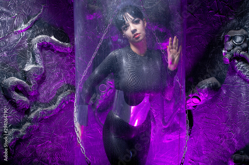 Shot of a futuristic young person posing behind glass space capsule with wires and purple neon light on black background