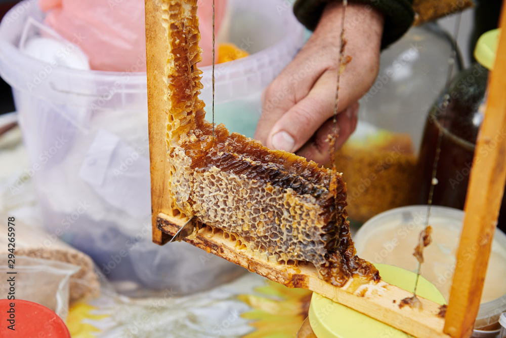 Man's hand cuts an appetizing piece of honeycomb with the knife. Selling homemade honey in the market. Degustation closeup. Honey farm.