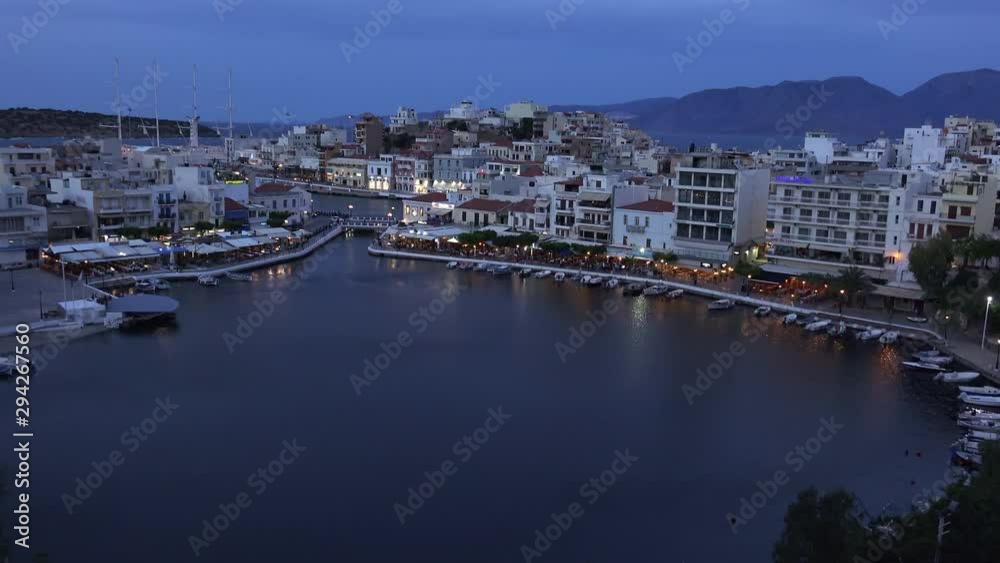 Beautiful sunset at Agios Nikolaos city, Port at Aegean sea. Crete,Greece. Peaceful harbor of Voulismeni Lake. Long promenade with restaurants. Panoramic view of seaport with yachts and boats at quay Beautiful sunset at Agios Nikolaos city, Port at Aegean sea. Crete,Greece. Peaceful harbor of Voulismeni Lake. Long promenade with restaurants. Panoramic view of seaport with yachts and boats at quay