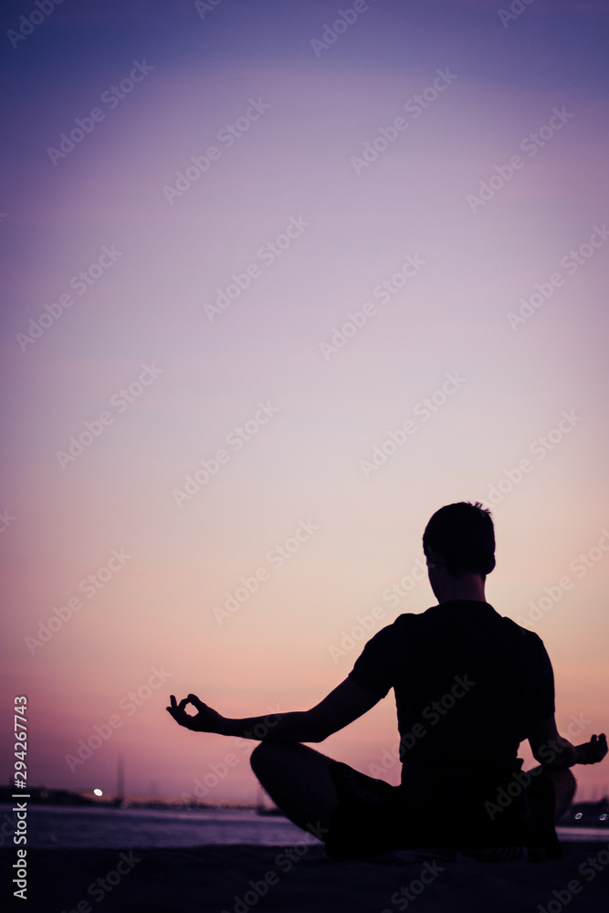 Silhouette of man doing yoga on the beach