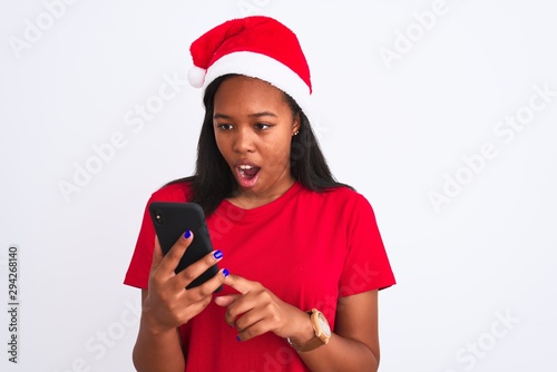 Young african american woman wearing christmas hat and using smartphone scared in shock with a surprise face, afraid and excited with fear expression © Krakenimages.com