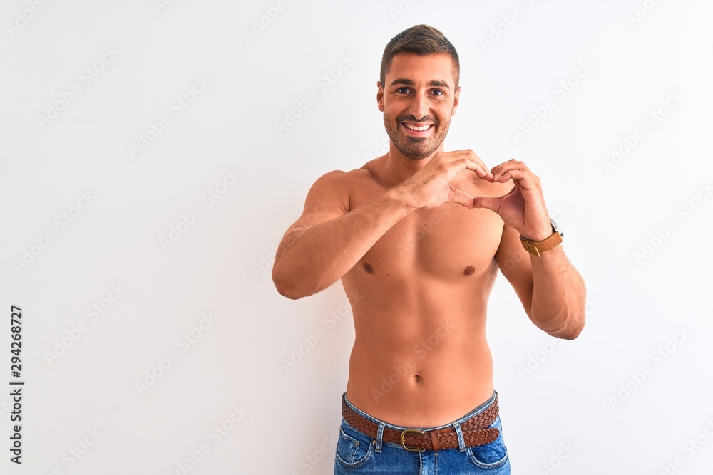 Young handsome shirtless man showing muscular body over isolated background smiling in love doing heart symbol shape with hands. Romantic concept.