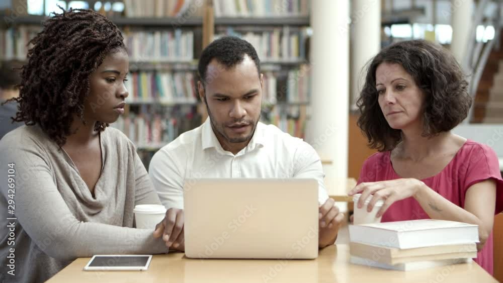 Serious mature students working with laptop at public library. Focused friends working over new task. Education concept Serious mature students working with laptop at public library. Focused friends working over new task. Education concept