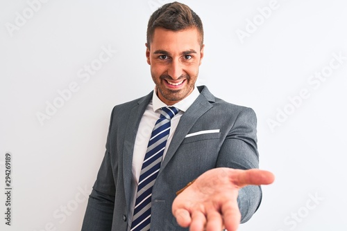Young handsome business man wearing suit and tie over isolated background smiling cheerful offering palm hand giving assistance and acceptance.