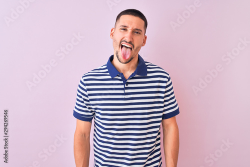 Young handsome man wearing nautical striped t-shirt over pink isolated background sticking tongue out happy with funny expression. Emotion concept.