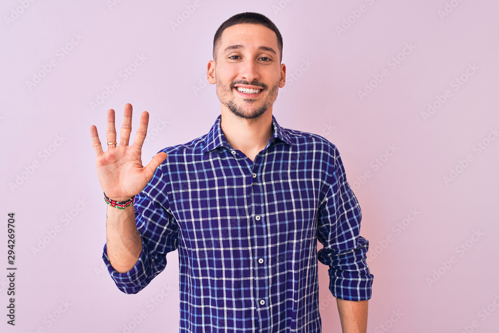 Naklejka premium Young handsome man standing over isolated background showing and pointing up with fingers number five while smiling confident and happy.