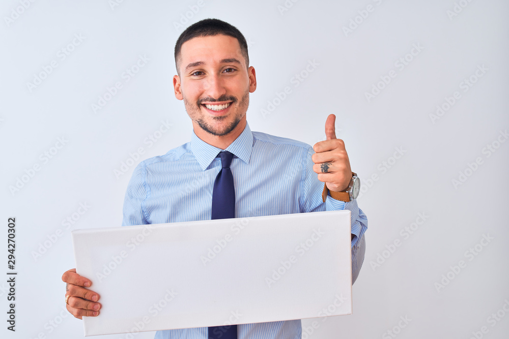 Young business man holding blank banner over isolated background happy with big smile doing ok sign, thumb up with fingers, excellent sign Young business man holding blank banner over isolated background happy with big smile doing ok sign, thumb up with fingers, excellent sign