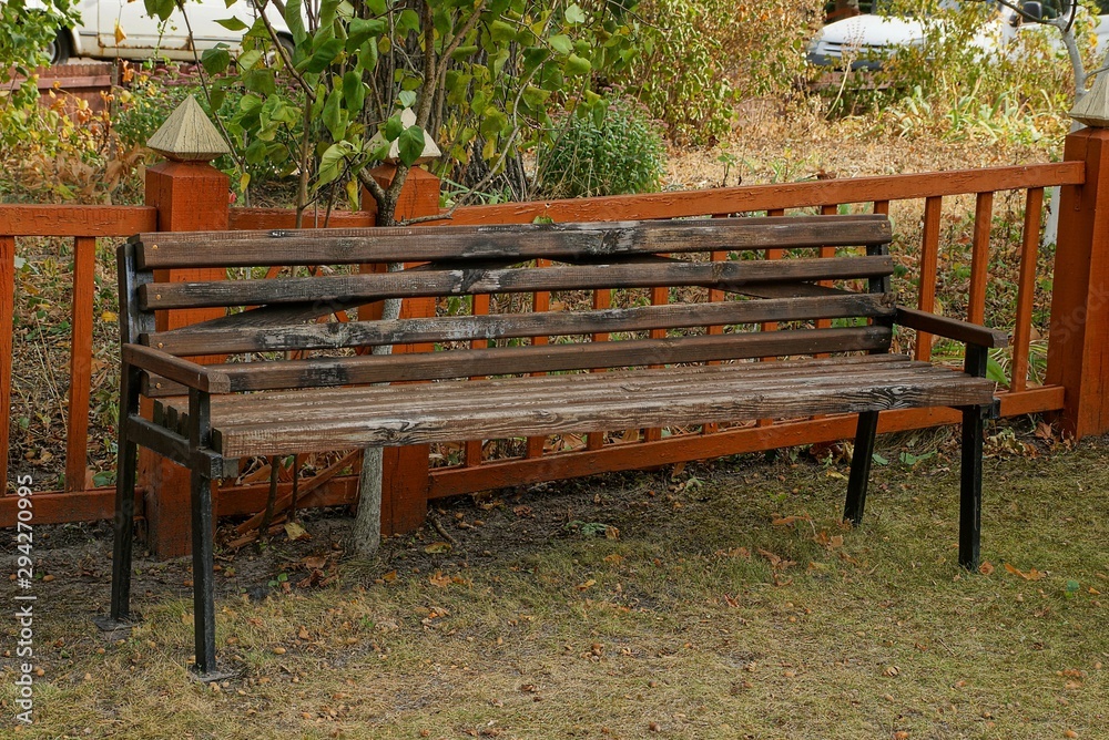 brown wooden bench stands on the ground near a decorative fence in the park brown wooden bench stands on the ground near a decorative fence in the park