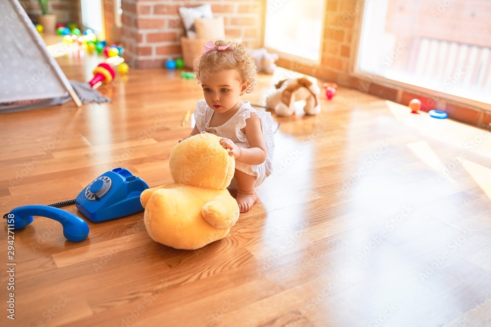 Fototapeta premium Beautiful caucasian infant playing with toys at colorful playroom. Happy and playful cuddling stuffed animal at kindergarten.