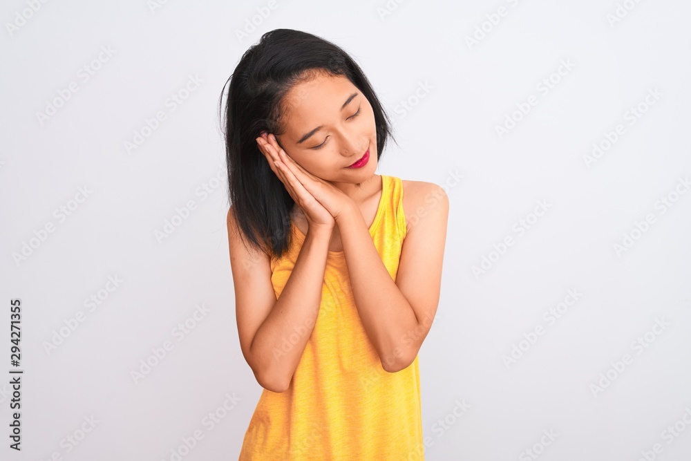 Young chinese woman wearing yellow casual t-shirt standing over isolated white background sleeping tired dreaming and posing with hands together while smiling with closed eyes. Young chinese woman wearing yellow casual t-shirt standing over isolated white background sleeping tired dreaming and posing with hands together while smiling with closed eyes.