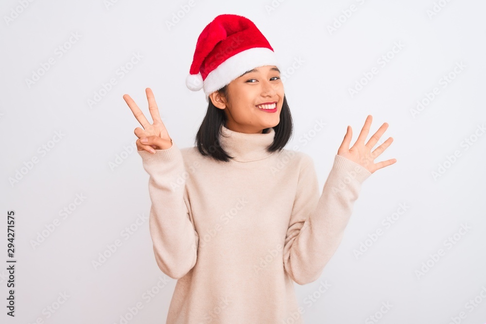 Young beautiful chinese woman wearing Christmas Santa hat over isolated white background showing and pointing up with fingers number seven while smiling confident and happy. Young beautiful chinese woman wearing Christmas Santa hat over isolated white background showing and pointing up with fingers number seven while smiling confident and happy.
