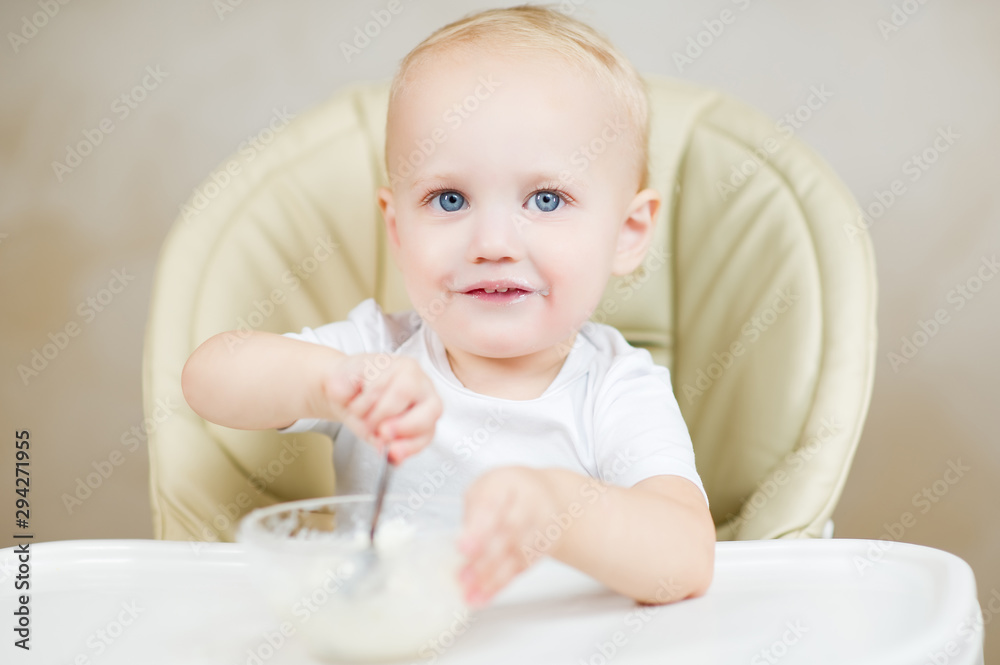 Smiling girl is picking up porridge with a spoon while sitting in a baby seat for feeding Smiling girl is picking up porridge with a spoon while sitting in a baby seat for feeding