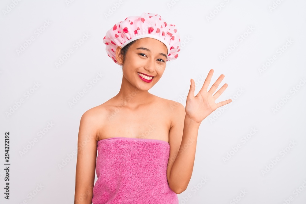 Young chinese woman wearing shower towel and cap bath over isolated white background showing and pointing up with fingers number five while smiling confident and happy. Young chinese woman wearing shower towel and cap bath over isolated white background showing and pointing up with fingers number five while smiling confident and happy.