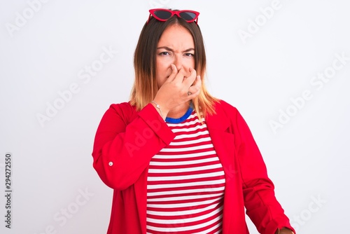 Young beautiful woman wearing striped t-shirt and jacket over isolated white background smelling something stinky and disgusting, intolerable smell, holding breath with fingers on nose