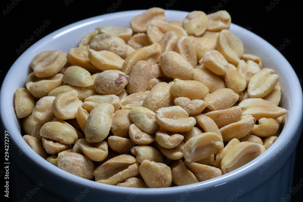 macro photography of shelled and salted peanuts in a white canister with black background macro photography of shelled and salted peanuts in a white canister with black background
